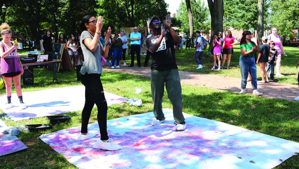 Andrea Muniz ‘21, left, and Antoine Williams, assistant professor of art, dance at Art on the Quad on Wednesday, Sept. 20. 2017. Muniz and Williams have bags on their feet that decorate a large canvas with chalk as they dance, an activity known as “Dance and Draw.”/Photo by Abigail Bekele/ The Guilfordian