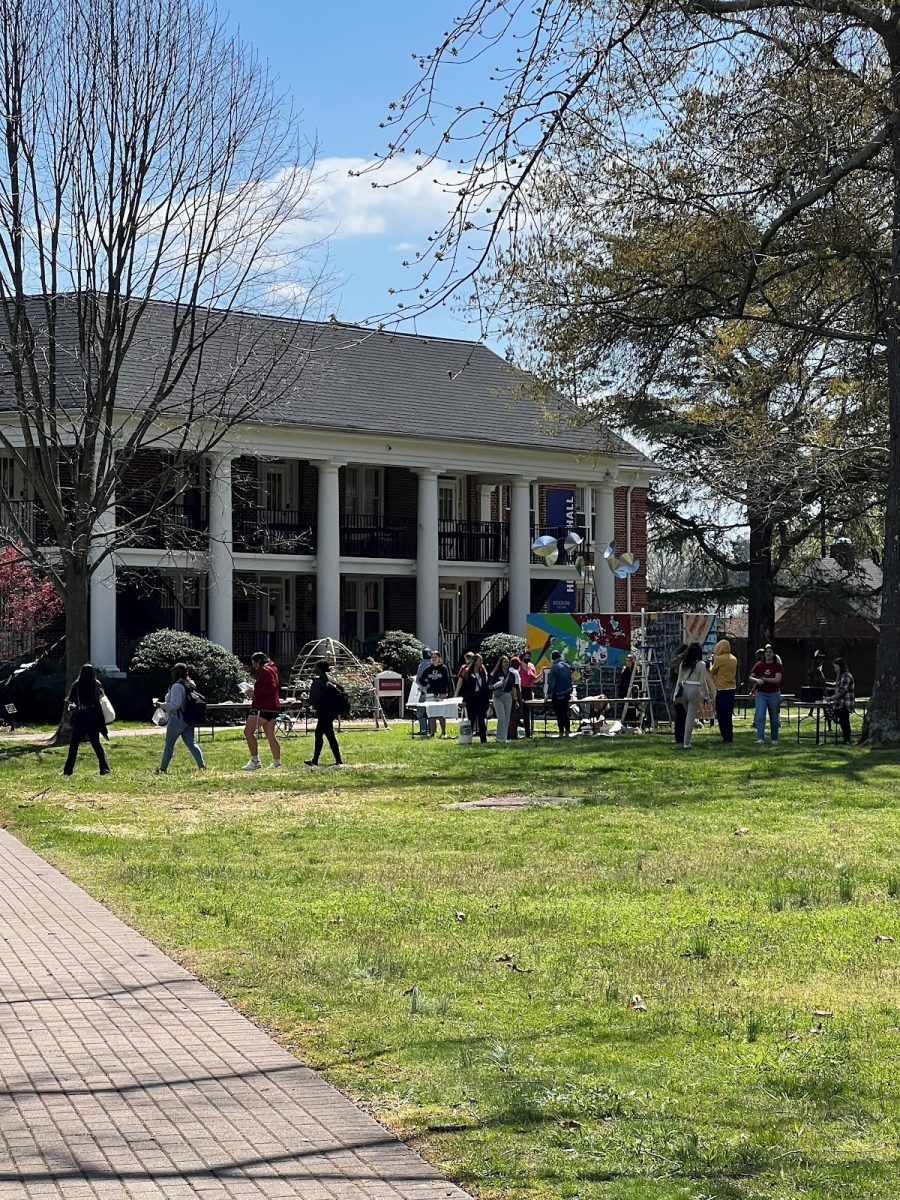 Students gathered outside of Hege-Cox Hall around tables displaying various ceramics and art prints for sale.